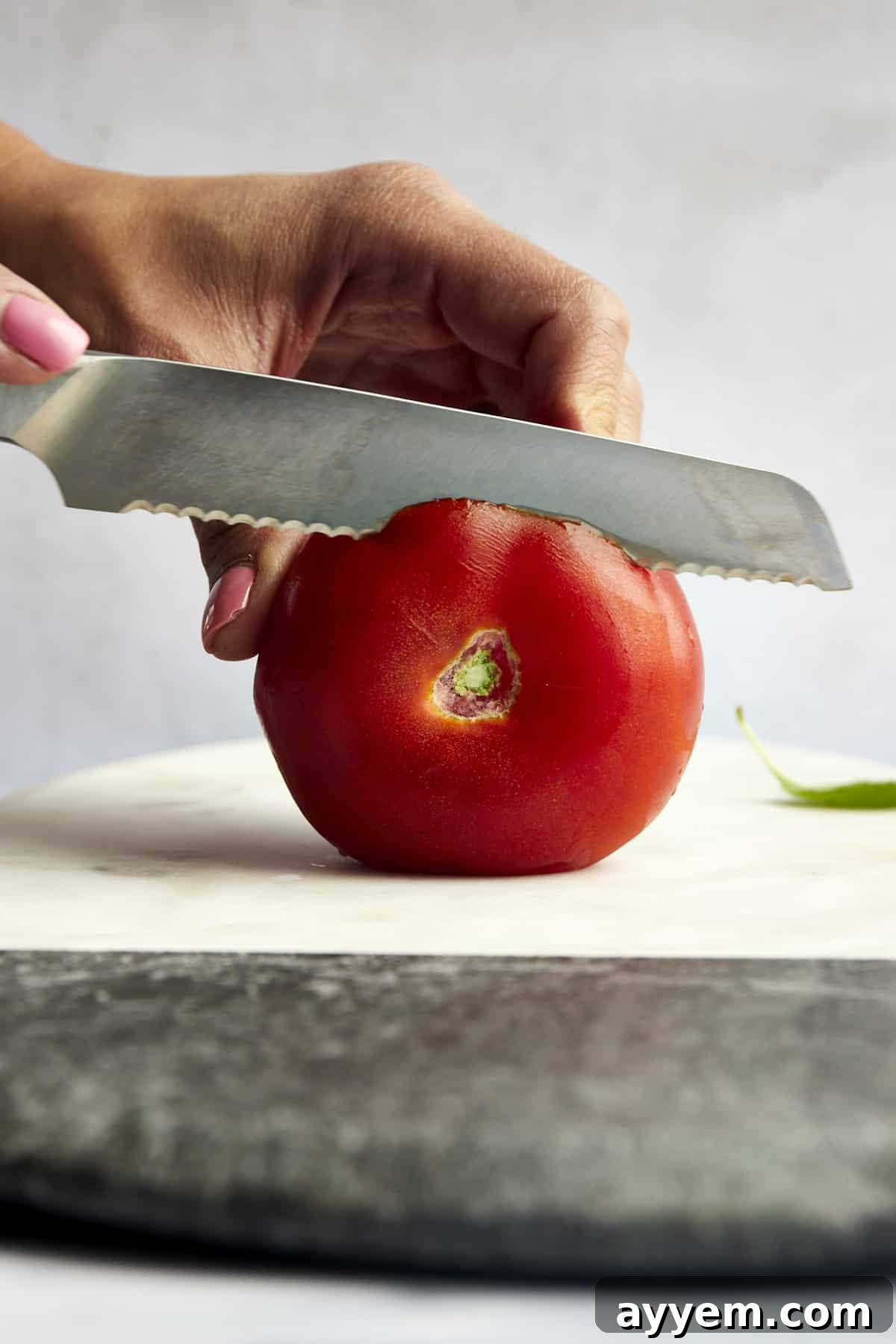 Mastering Tomato Slices Three Essential Techniques 8 A side view of the top of a tomato being sliced off.