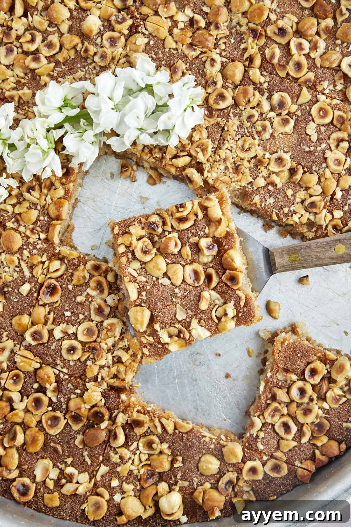 A golden piece of Basbousa, a Middle Eastern semolina cake, being lifted from a pan, showing its moist texture.