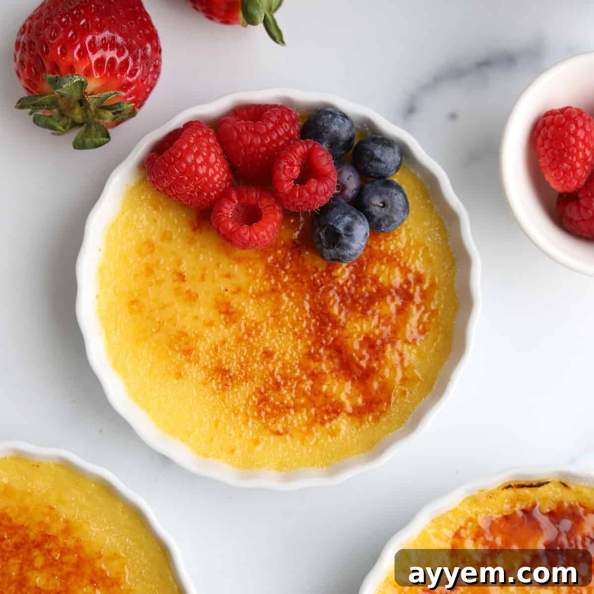 Overhead image of a beautifully caramelized pot of Crème Brûlée, topped with fresh berries, inviting a spoonful.