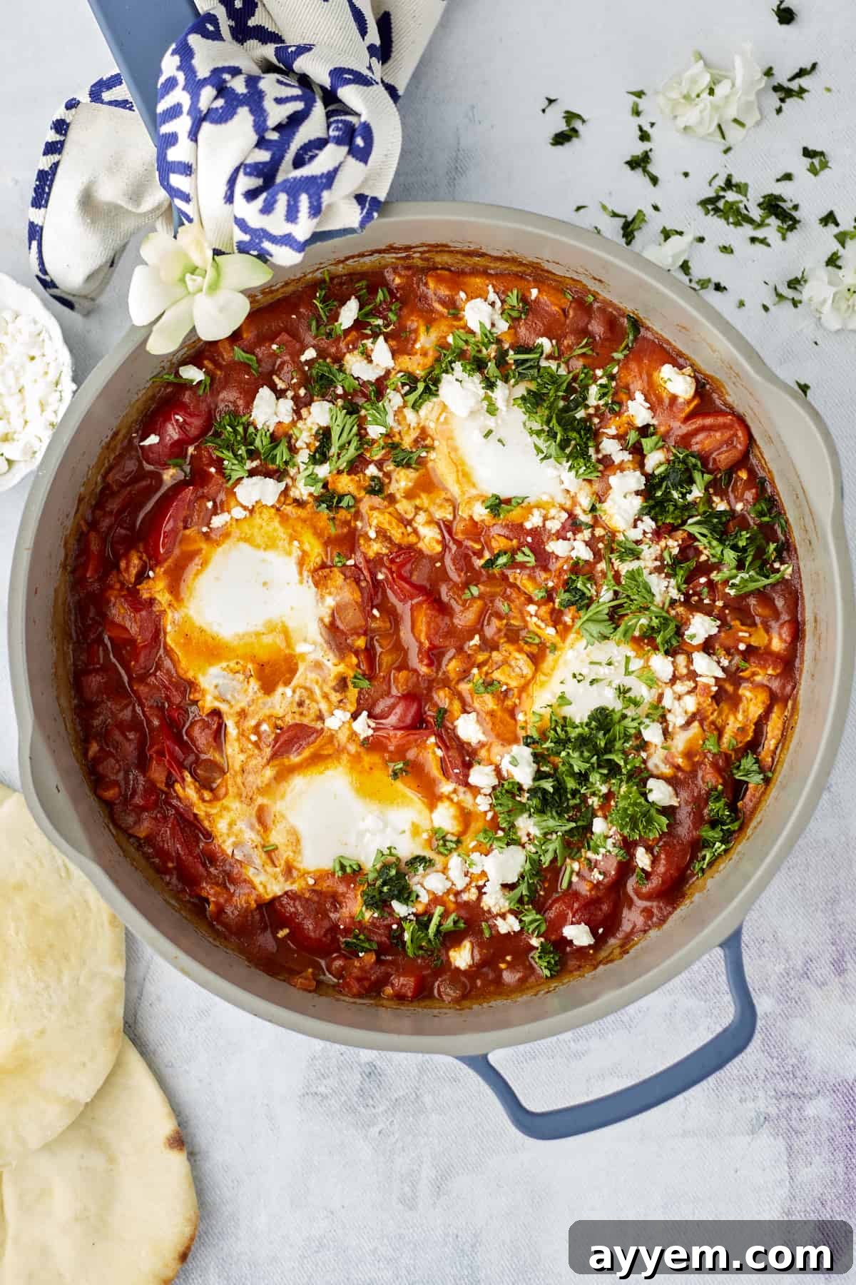 A rustic cast iron pan filled with shakshuka, garnished with fresh herbs, ready for dipping.