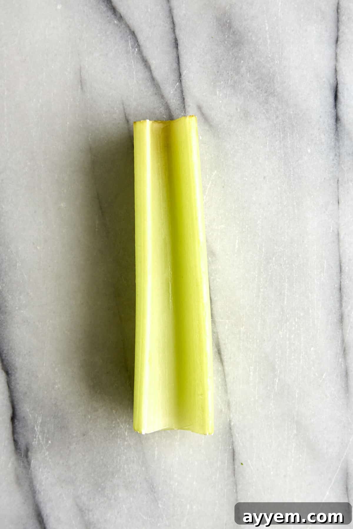 A fresh, green celery stick, ready for preparation. Highlight the crisp texture and natural freshness.
