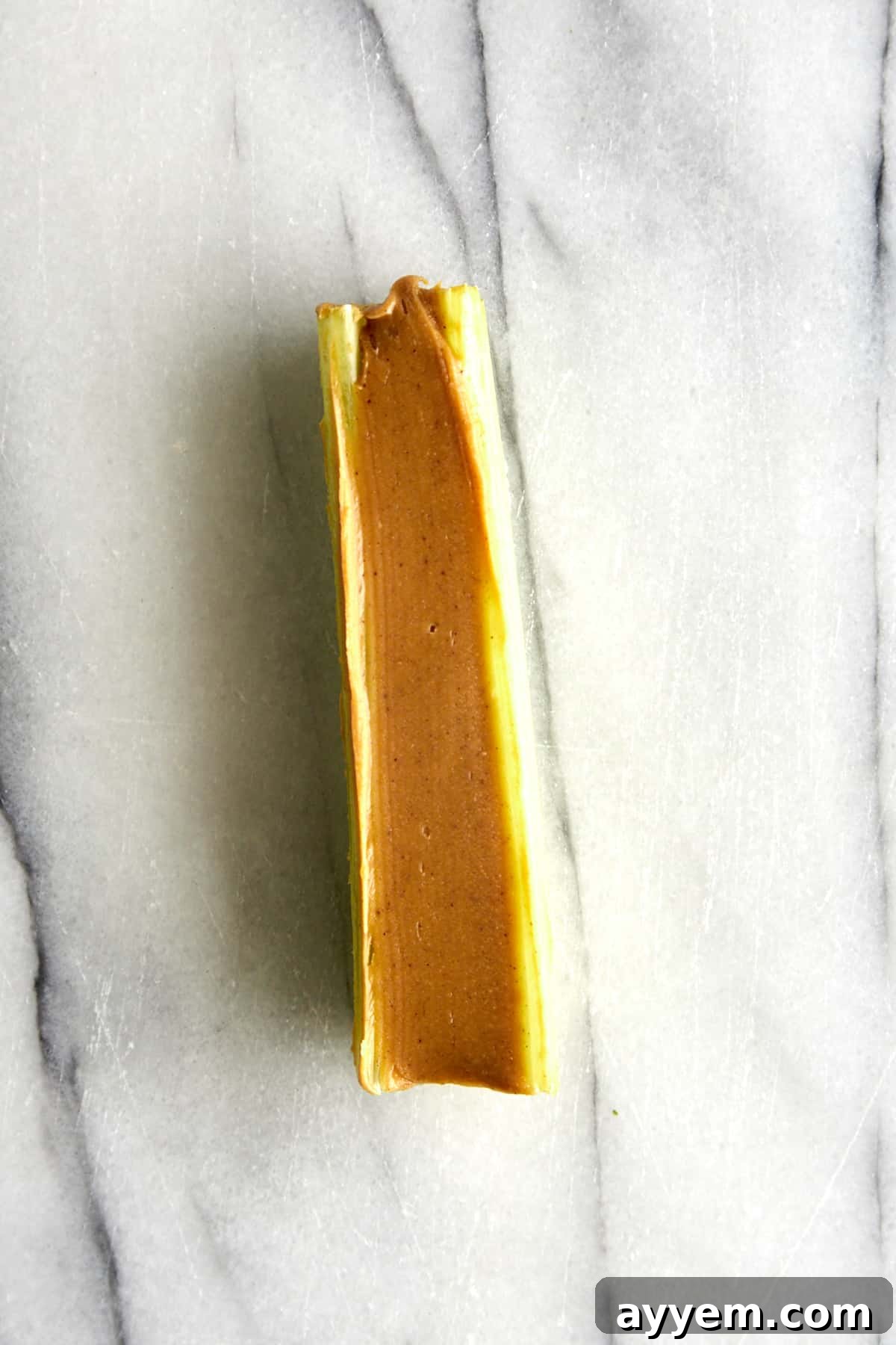 A celery stick generously filled with creamy peanut butter, showing the satisfying texture. This step prepares the celery for its chocolate dip.