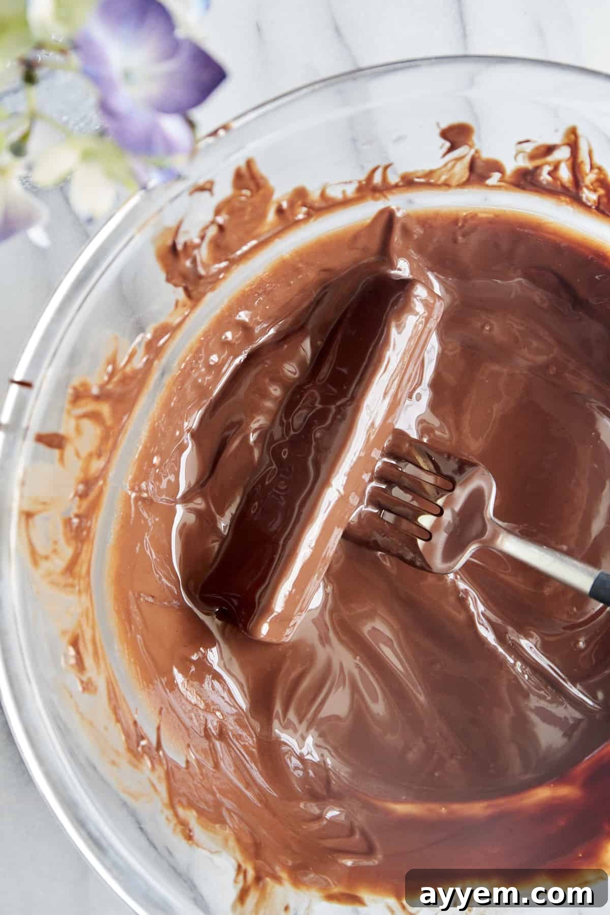 Overhead image of a fork gently rolling a peanut butter stuffed celery stick in a bowl of melted chocolate. This highlights the dipping process for the chocolate coating.