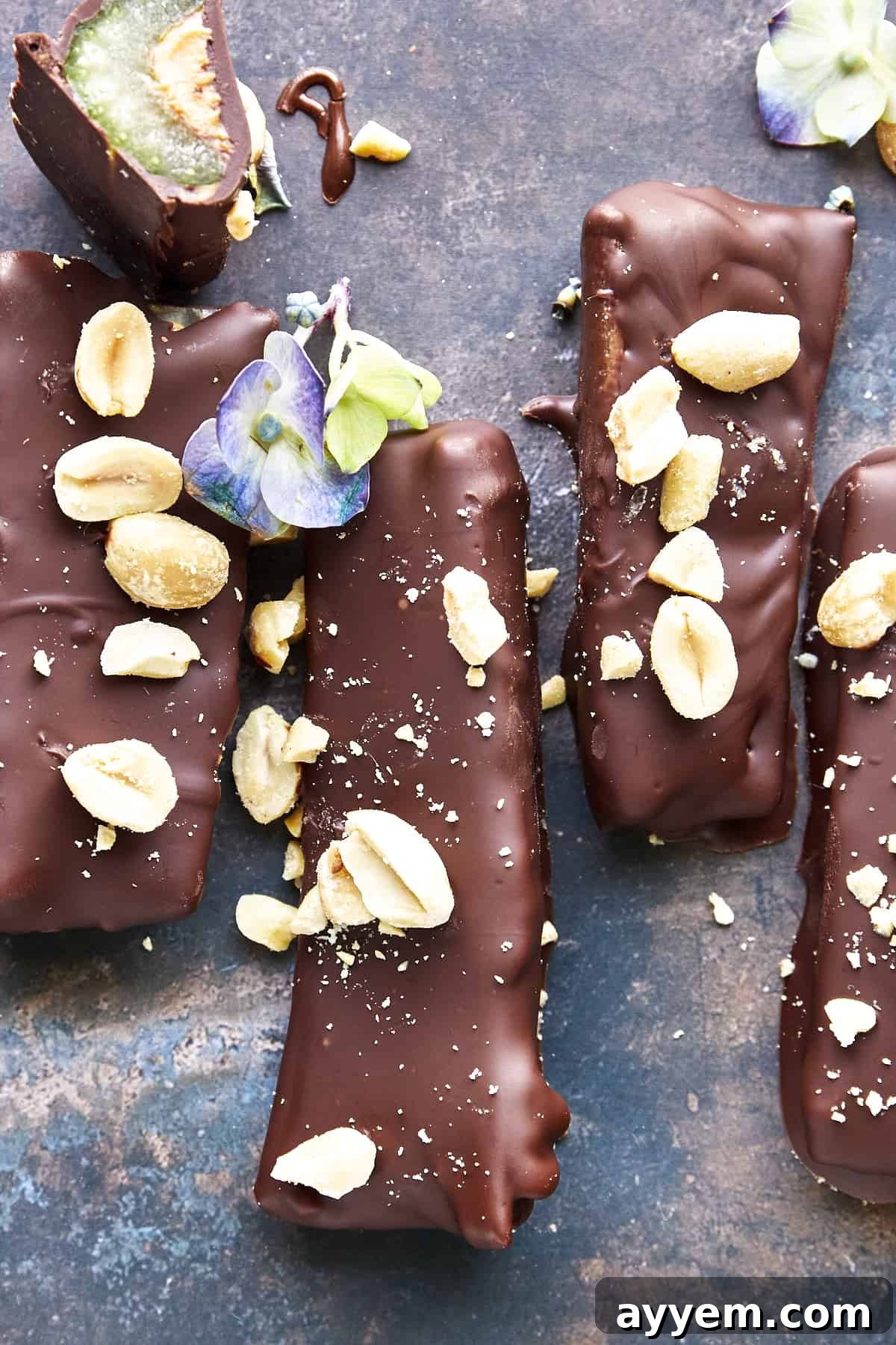 A vibrant display of four full-sized chocolate celery and peanut butter logs, elegantly garnished with crushed peanuts and sea salt. A fifth log, with a delightful bite missing, showcases the irresistible layers of this healthy snack.