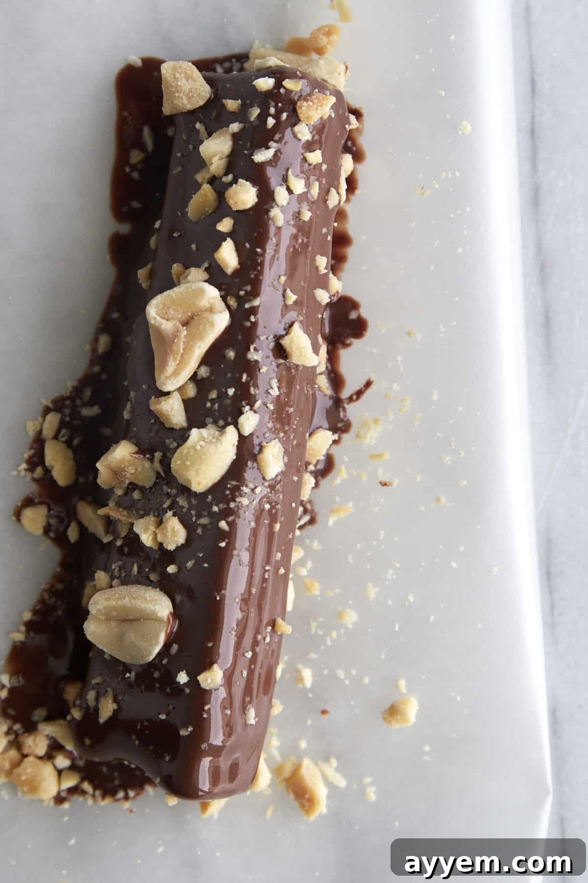 An individual celery stick, perfectly coated in wet chocolate and adorned with peanuts and sea salt, carefully placed on a piece of parchment paper to set. This image highlights the crucial chilling step.