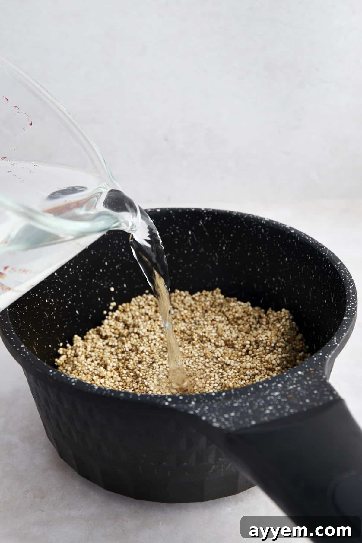 Water being poured into a pot full of uncooked white quinoa, preparing for stovetop cooking.