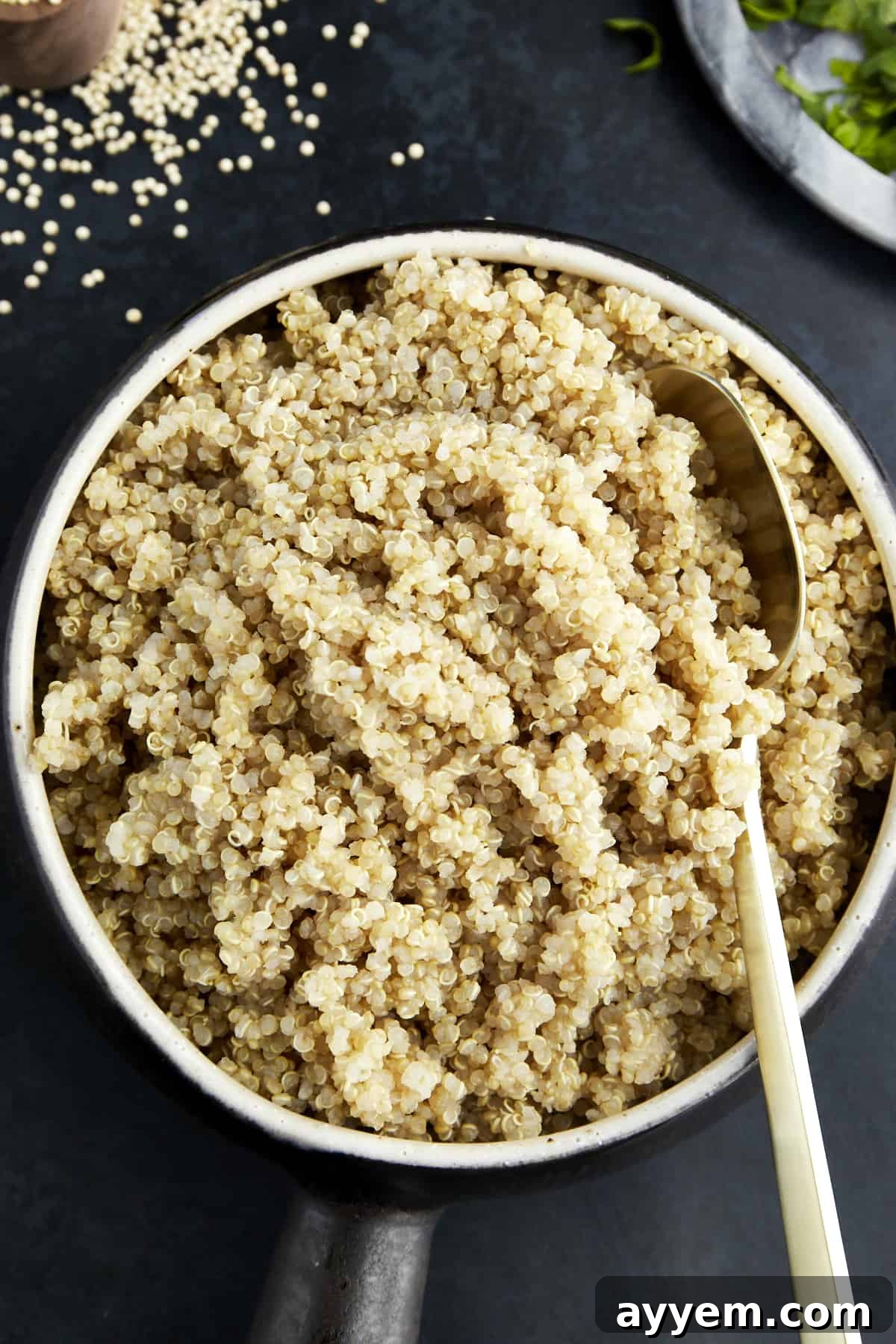 A bowl of cooked quinoa with a spoon sticking out, garnished with fresh herbs.
