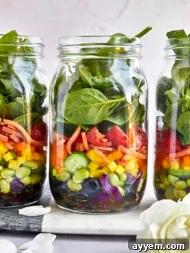 Three healthy rainbow salad jars, layered with colorful fruits and vegetables.