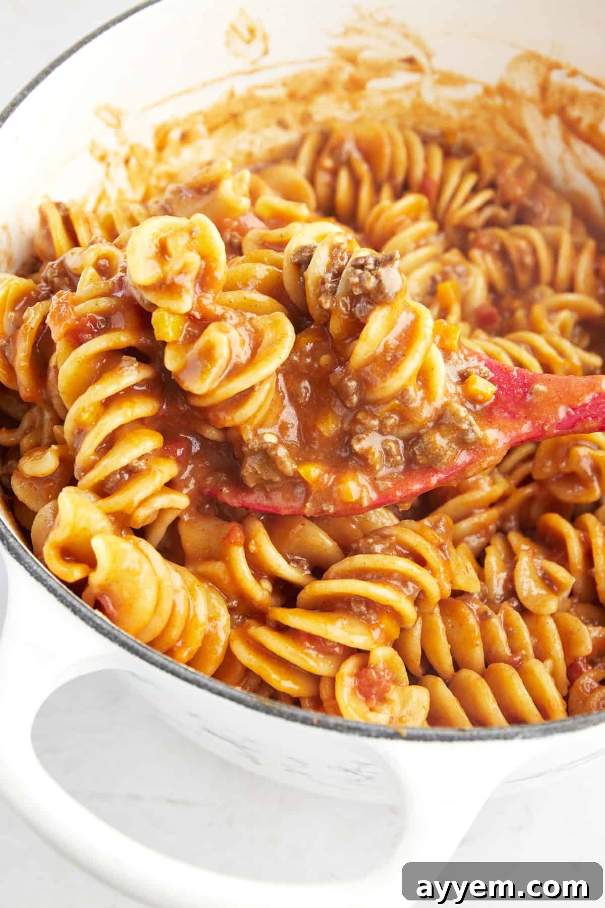 A rubber spoon stirring cooked taco pasta in a pot. 