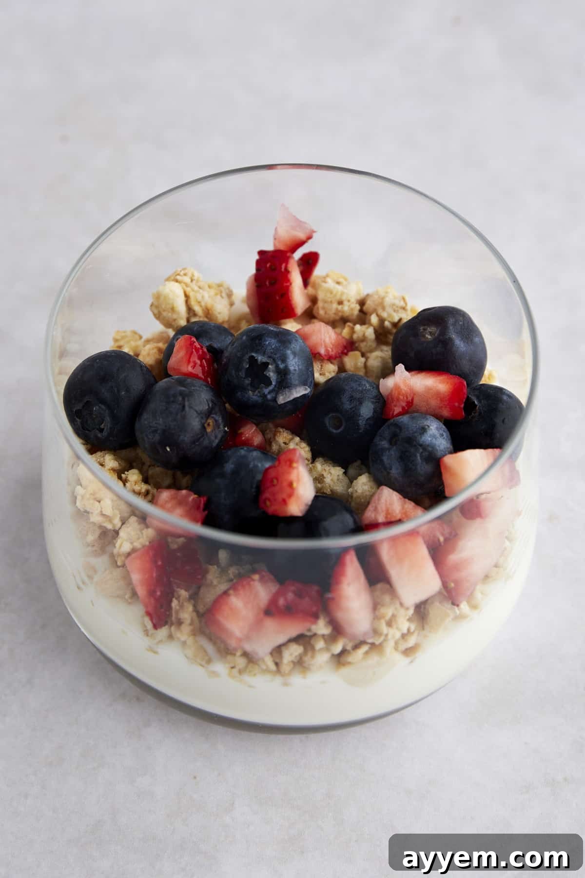 A glass jar with yogurt, granola, chopped strawberries, and blueberries, demonstrating the layered parfait assembly.