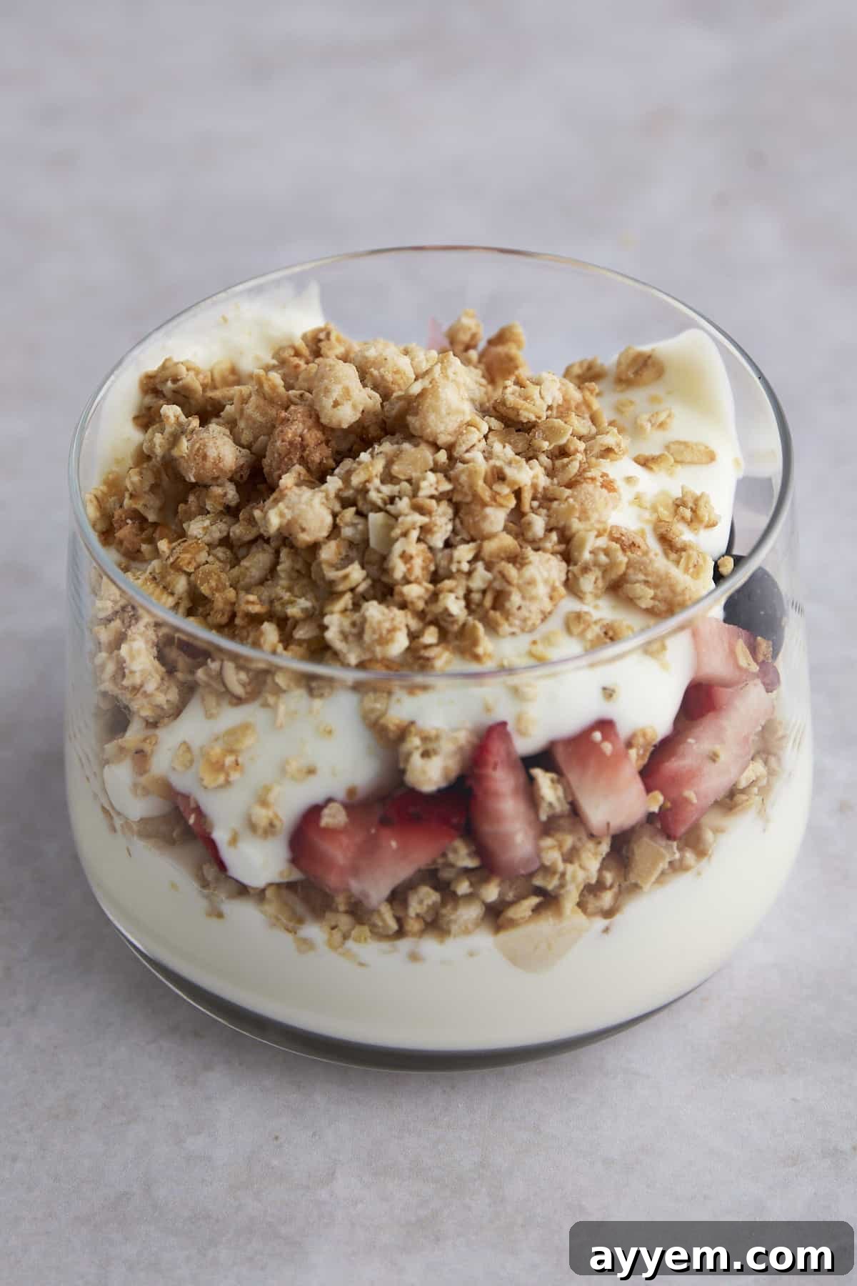 Side view of a fruit and yogurt parfait with yogurt, strawberries and granola, ready for storage.