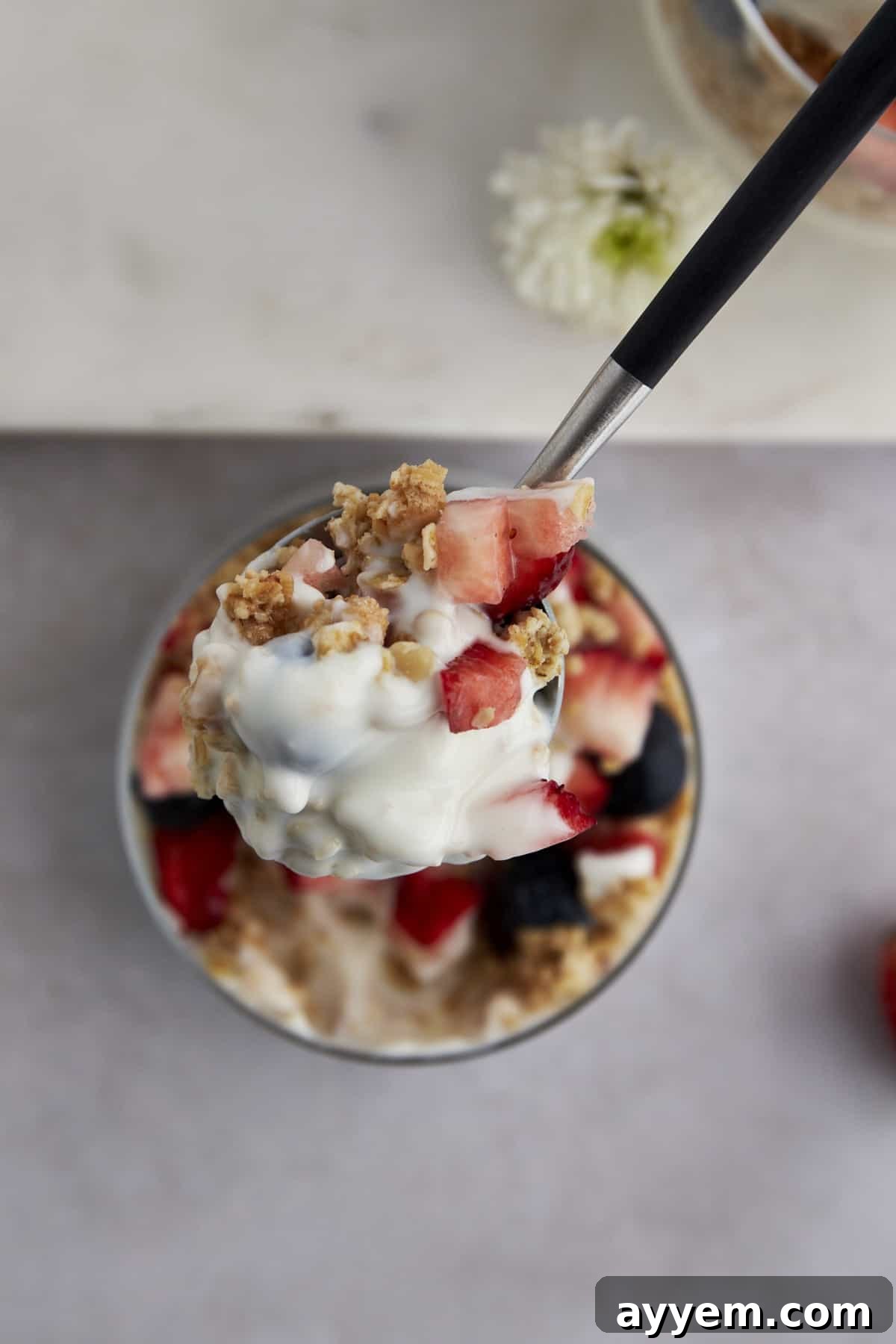 A spoonful of a yogurt parfait with granola, blueberries, and strawberries, ready to be enjoyed.