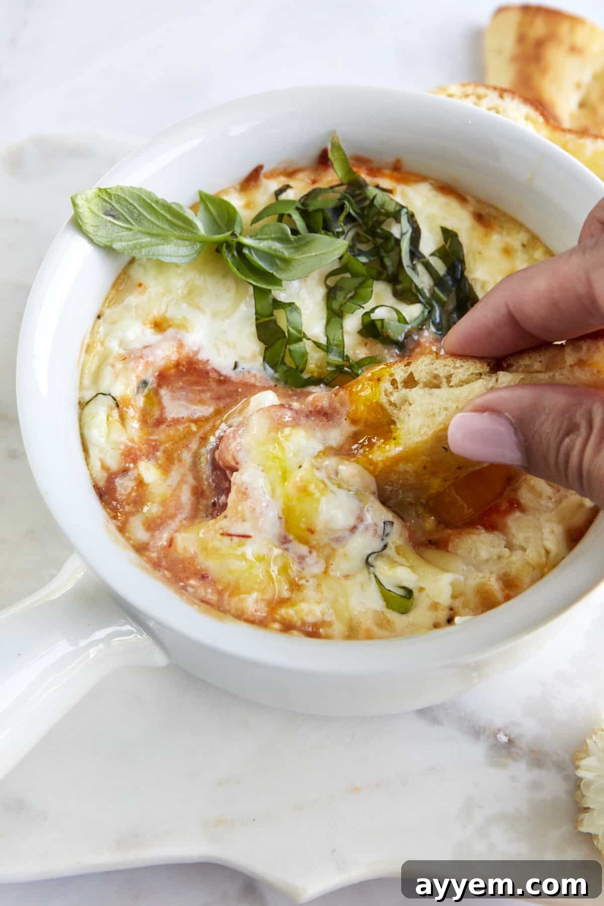 Easy Italian Baked Eggs Purgatorio 5 Two fingers dipping a piece of bread into a ramekin full of Eggs in Purgatory.