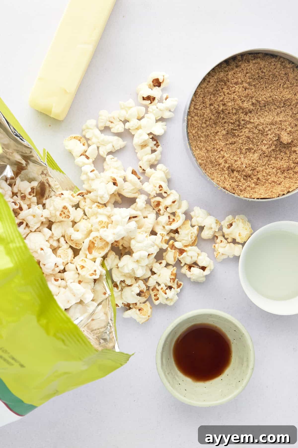Key ingredients for homemade caramel popcorn: freshly popped popcorn, a stick of butter, brown sugar, corn syrup, and vanilla extract.
