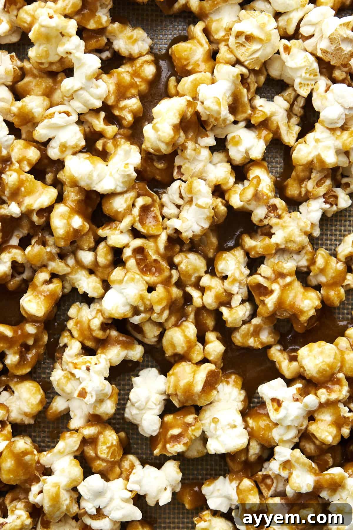 Golden caramel sauce being poured evenly over a bed of freshly popped popcorn on a baking sheet, ready for baking.