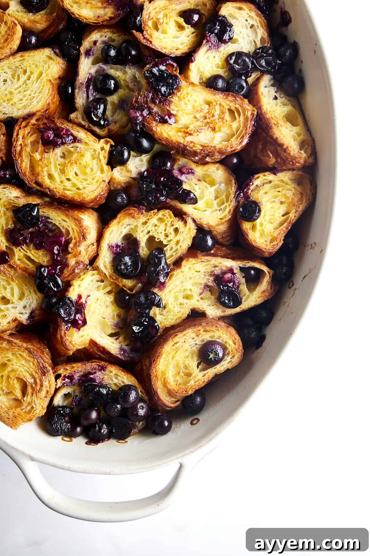 Overhead image of croissant pieces in a baking dish with blueberries on top. 