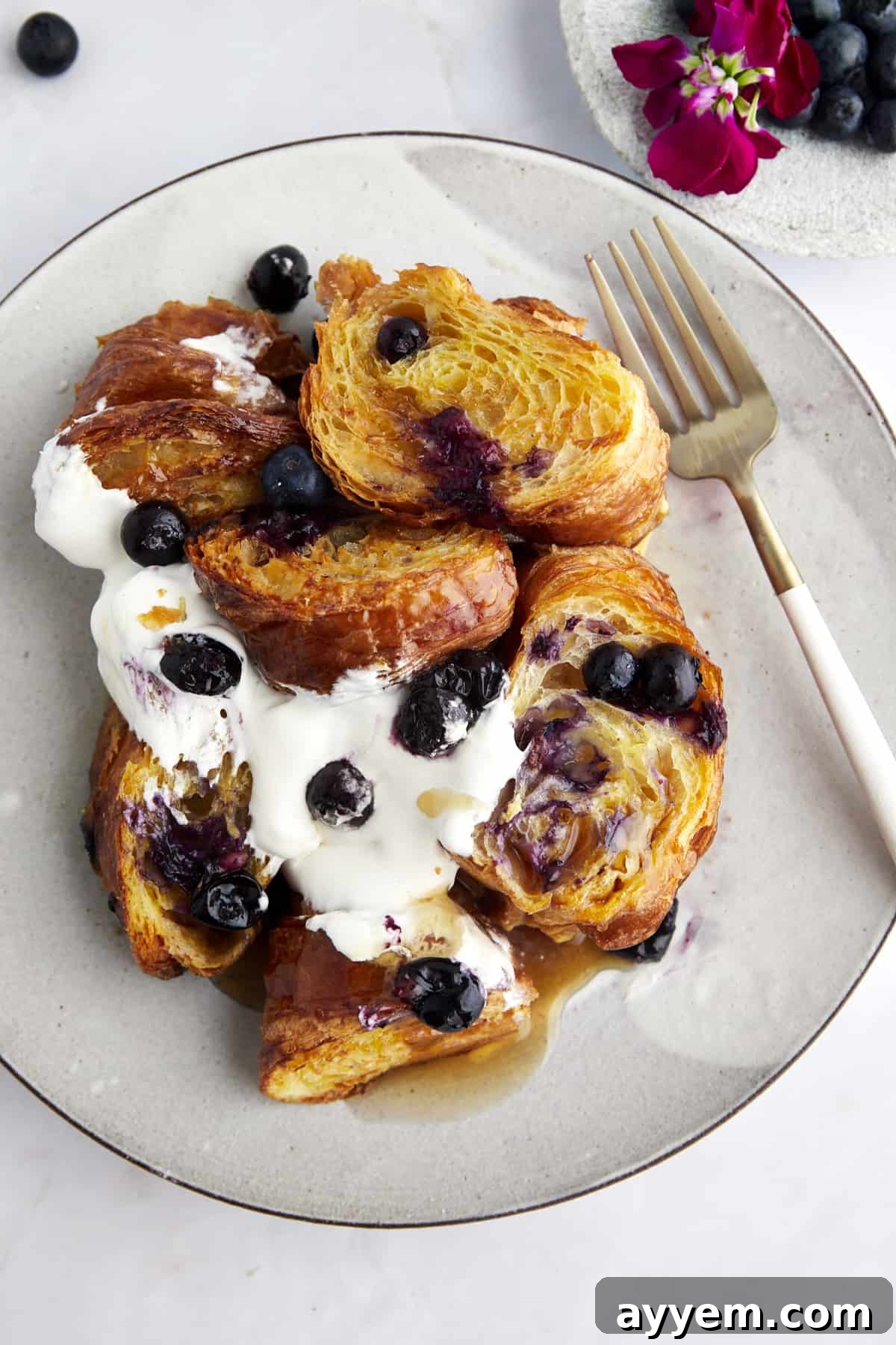 A plate of croissant blueberry French toast topped with yogurt, blueberries,  and syrup. 