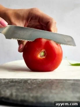 A close-up side view of a ripe red tomato being expertly sliced, demonstrating a basic kitchen skill