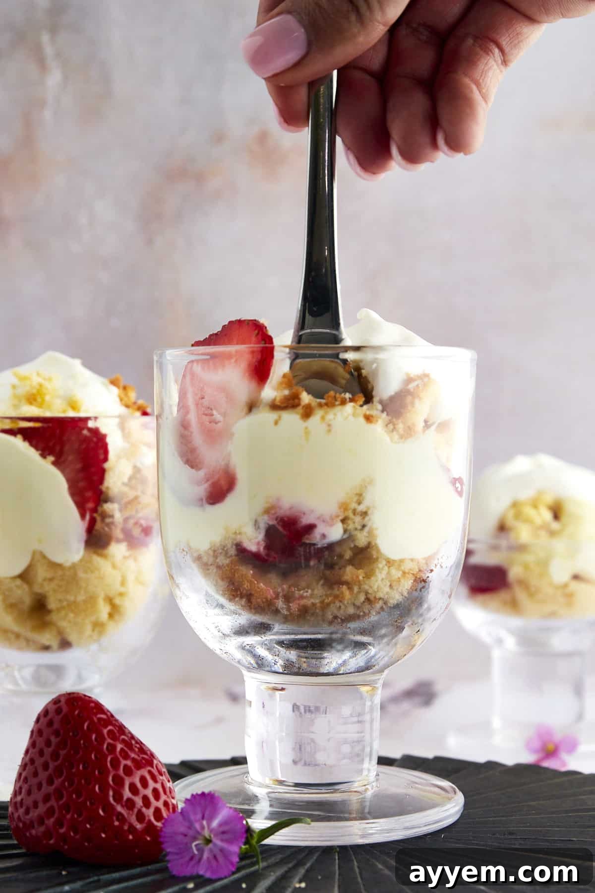 A hand holding a fork delving into the creamy, fruity layers of a strawberry shortcake shooter.