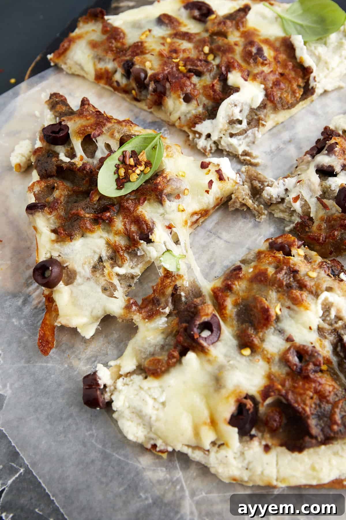A perfectly sliced Feta Gyro Pizza, showcasing its golden crust, melted mozzarella, savory gyro meat, and creamy whipped feta base, garnished with fresh herbs and a sprinkle of red pepper flakes.