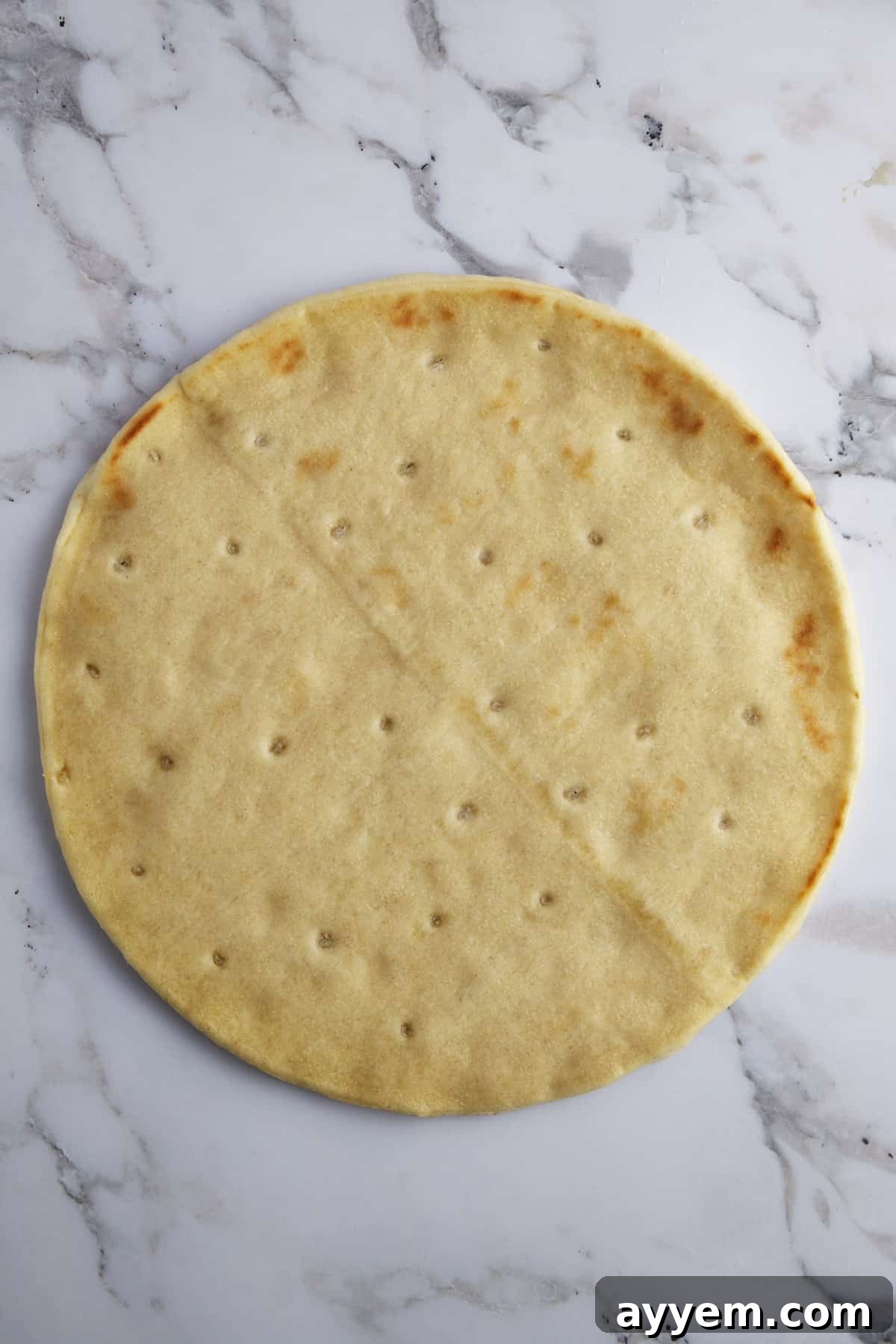 A round, raw pizza crust, lightly dusted with flour, laid out on a baking surface, ready for toppings.