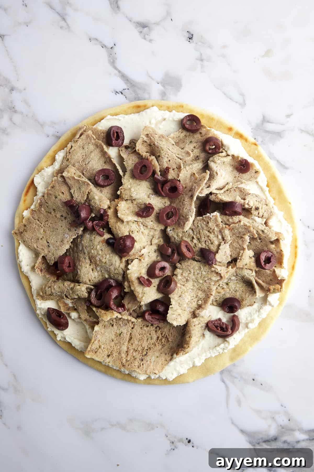 Pizza crust with whipped feta, gyro meat, and scattered Kalamata olives, adding a briny touch.