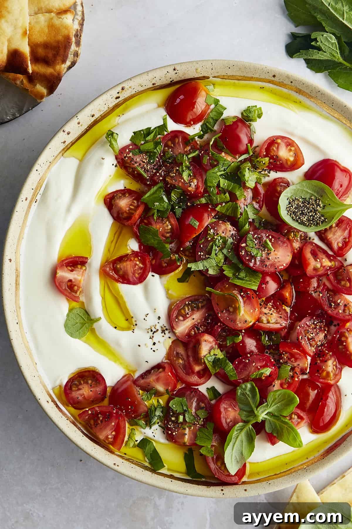 A beautifully arranged bowl of Marinated Tomatoes and Whipped Feta Dip, garnished with fresh herbs and a generous drizzle of olive oil.