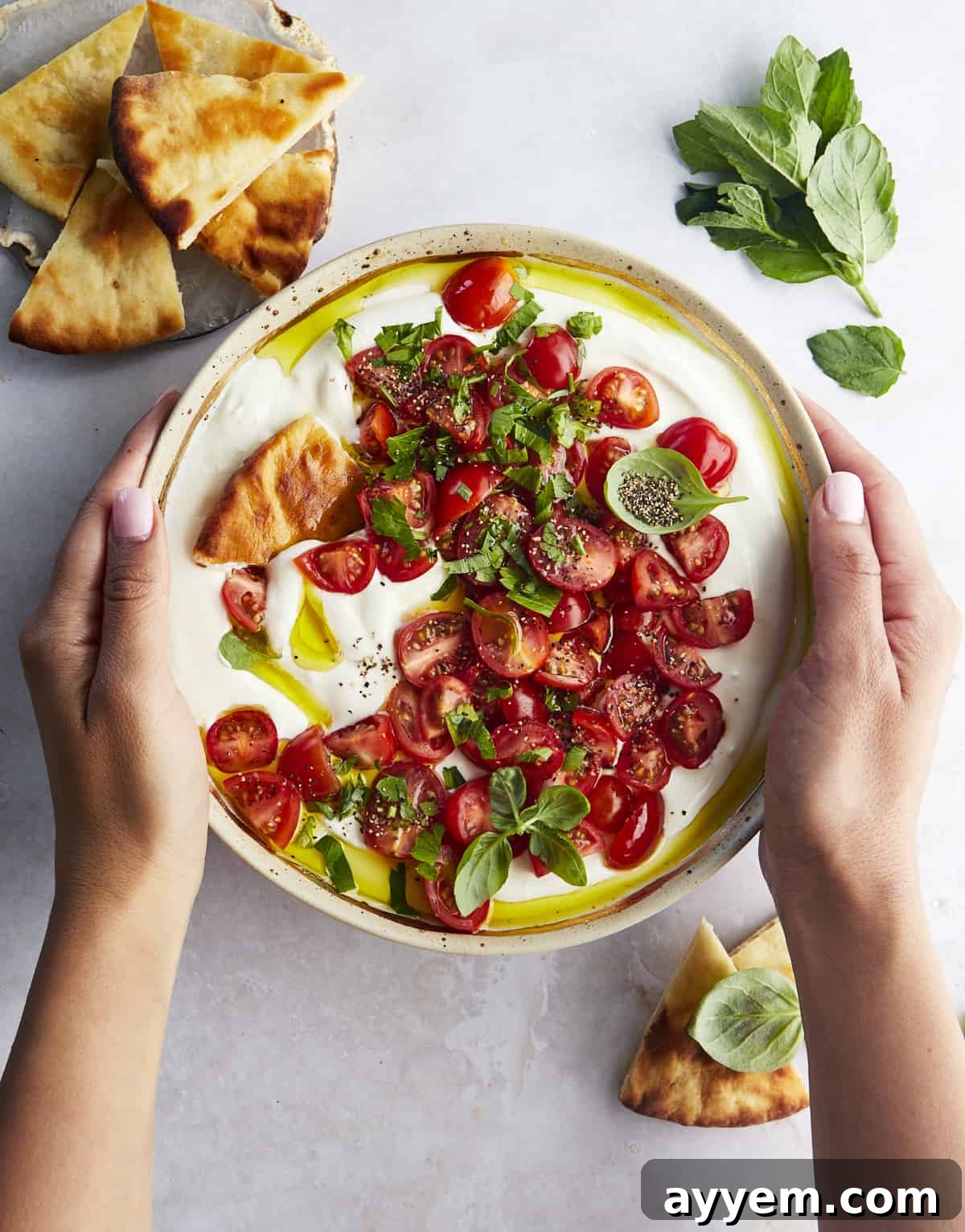Two hands reaching for a serving of Marinated Tomatoes and Whipped Feta Dip with warm pita bread.