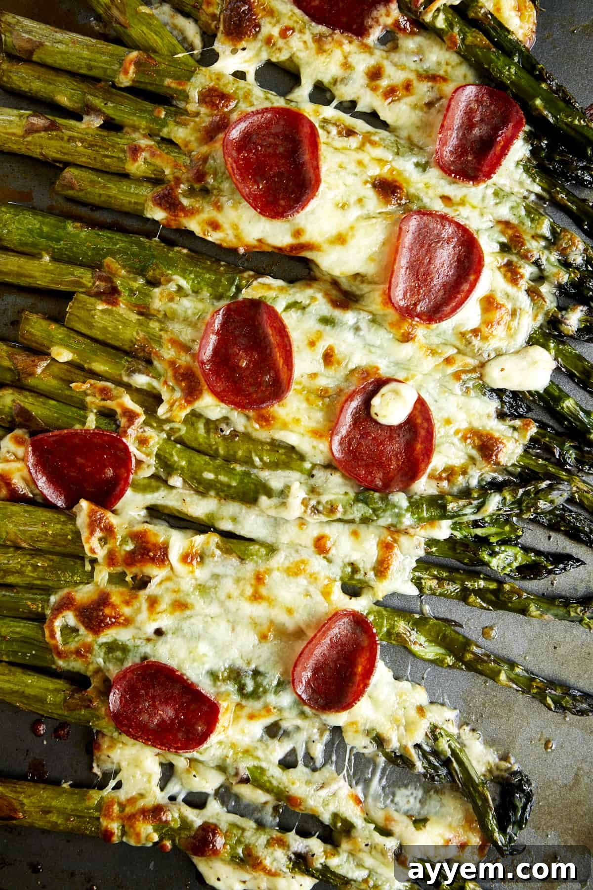 Overhead image of oven roasted asparagus topped with cheese and pepperoni. 