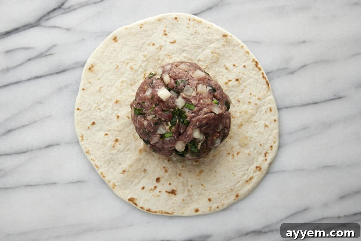 Seasoned ground beef patty on top of a tortilla. 