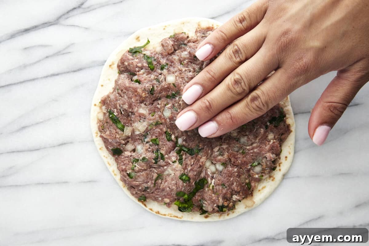 A hand smashing seasoned ground beef onto a tortilla. 