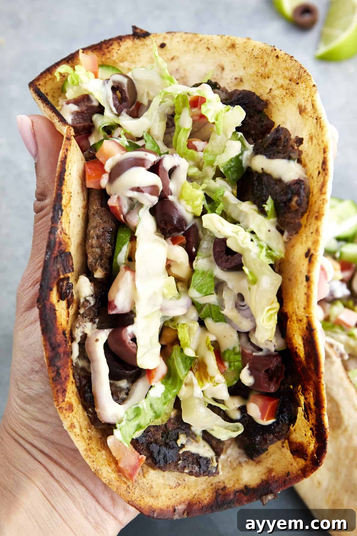 A hand holding a folded Greek-inspired smashed taco. 