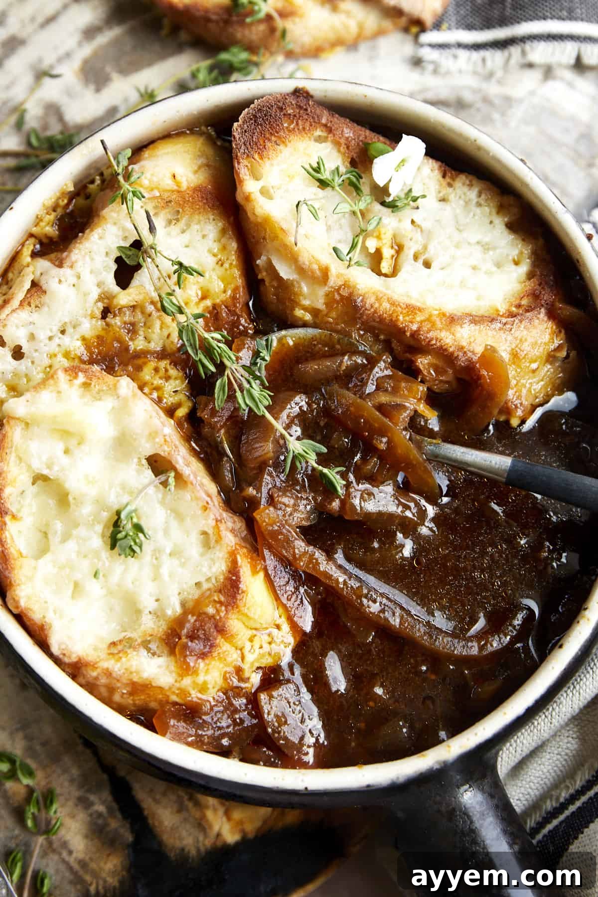 A close-up of a spoon dipping into a bowl of easy French onion soup, showing the melted cheese, broth, and onions.