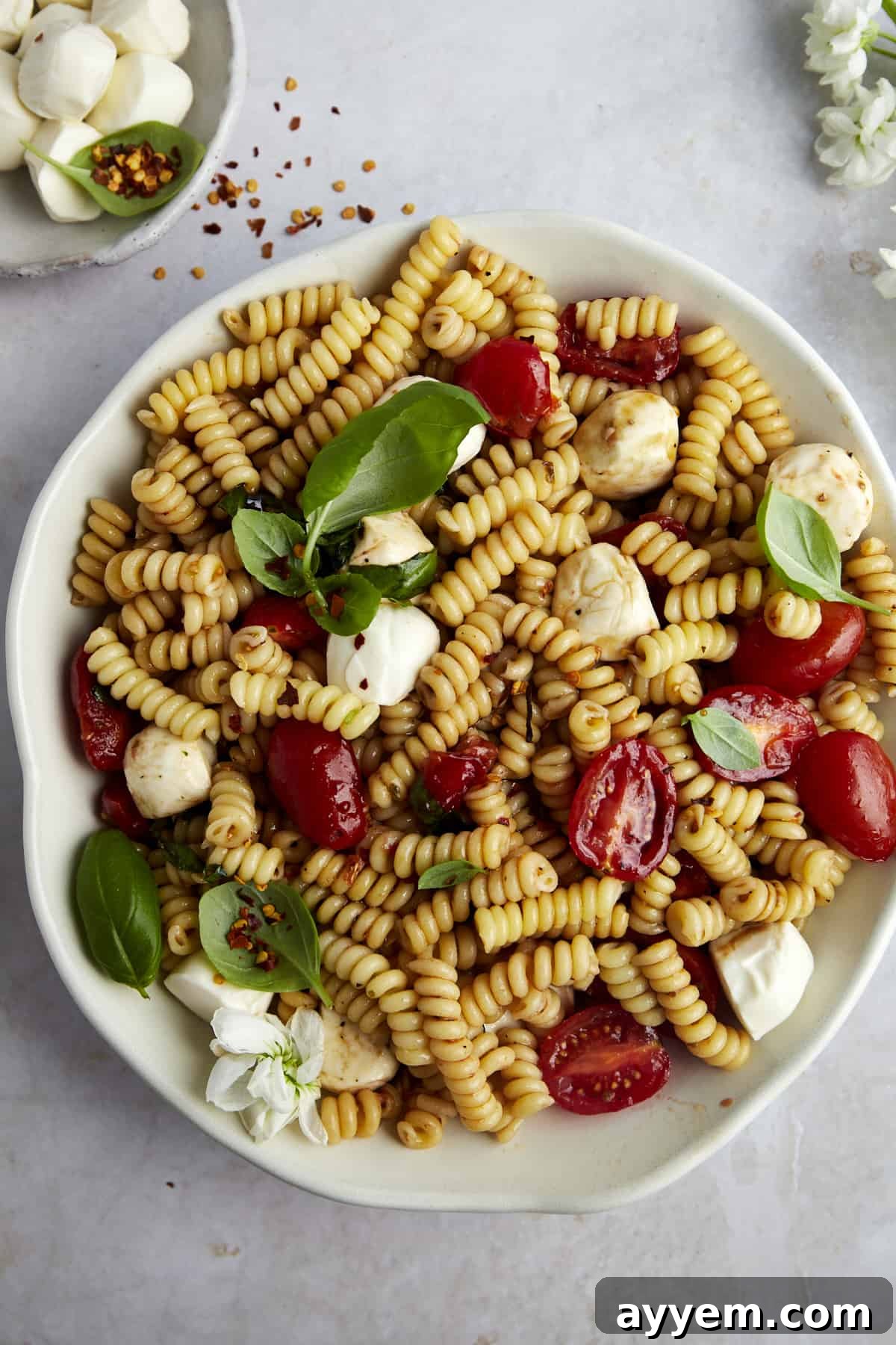 Overhead image of a bowl of colorful Caprese pasta salad, showcasing fresh mozzarella, ripe tomatoes, and basil leaves.