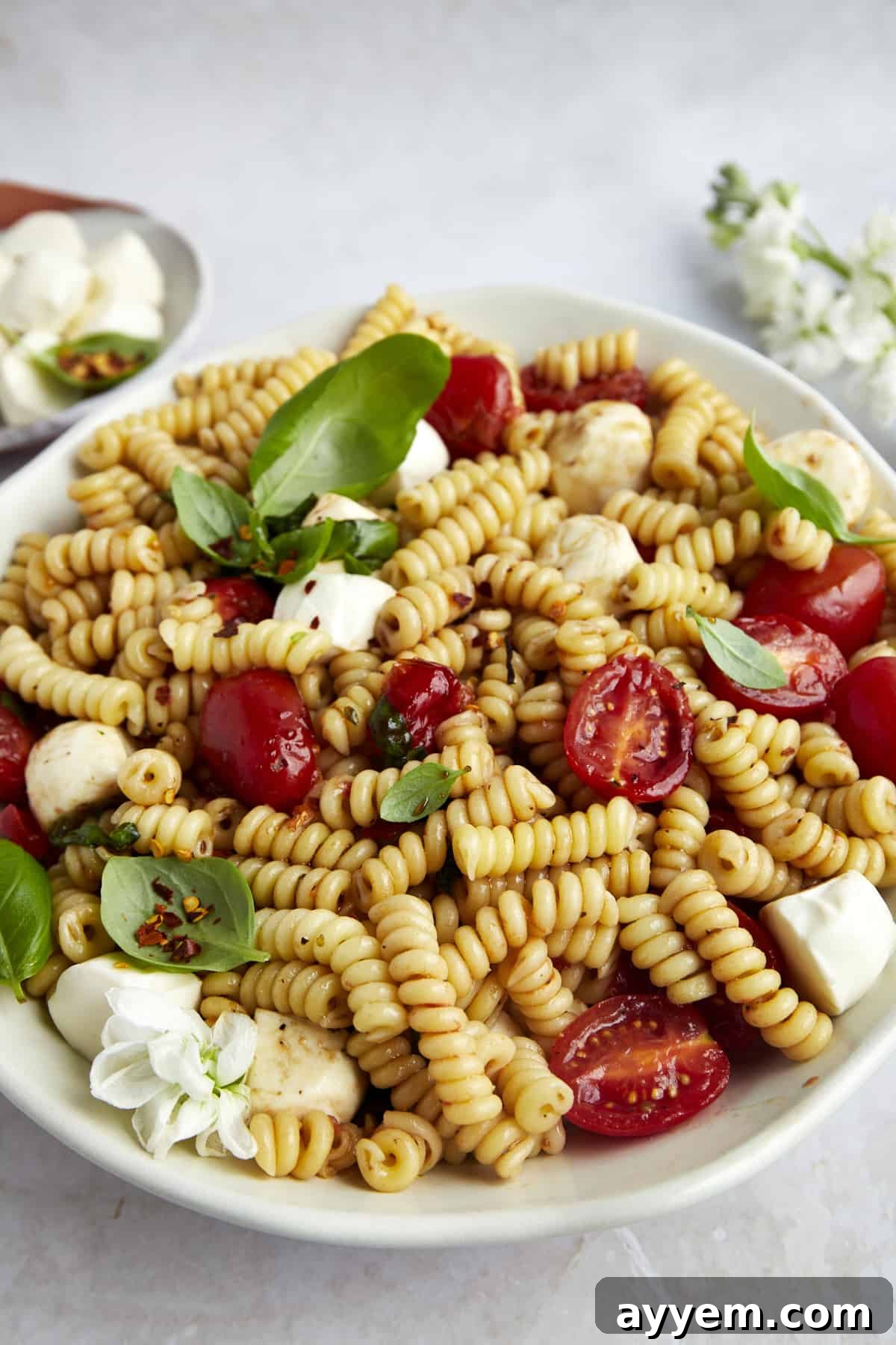 A bowl of Caprese pasta salad glistening with balsamic glaze and topped with fresh basil leaves.