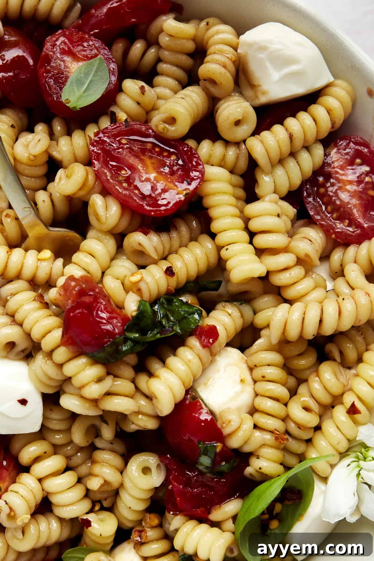 Close-up image of a vibrant bowl of Caprese pasta salad, highlighting the fresh ingredients and glossy balsamic glaze.