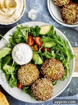 a salad topped with three falafel balls and a bowl of tzatziki