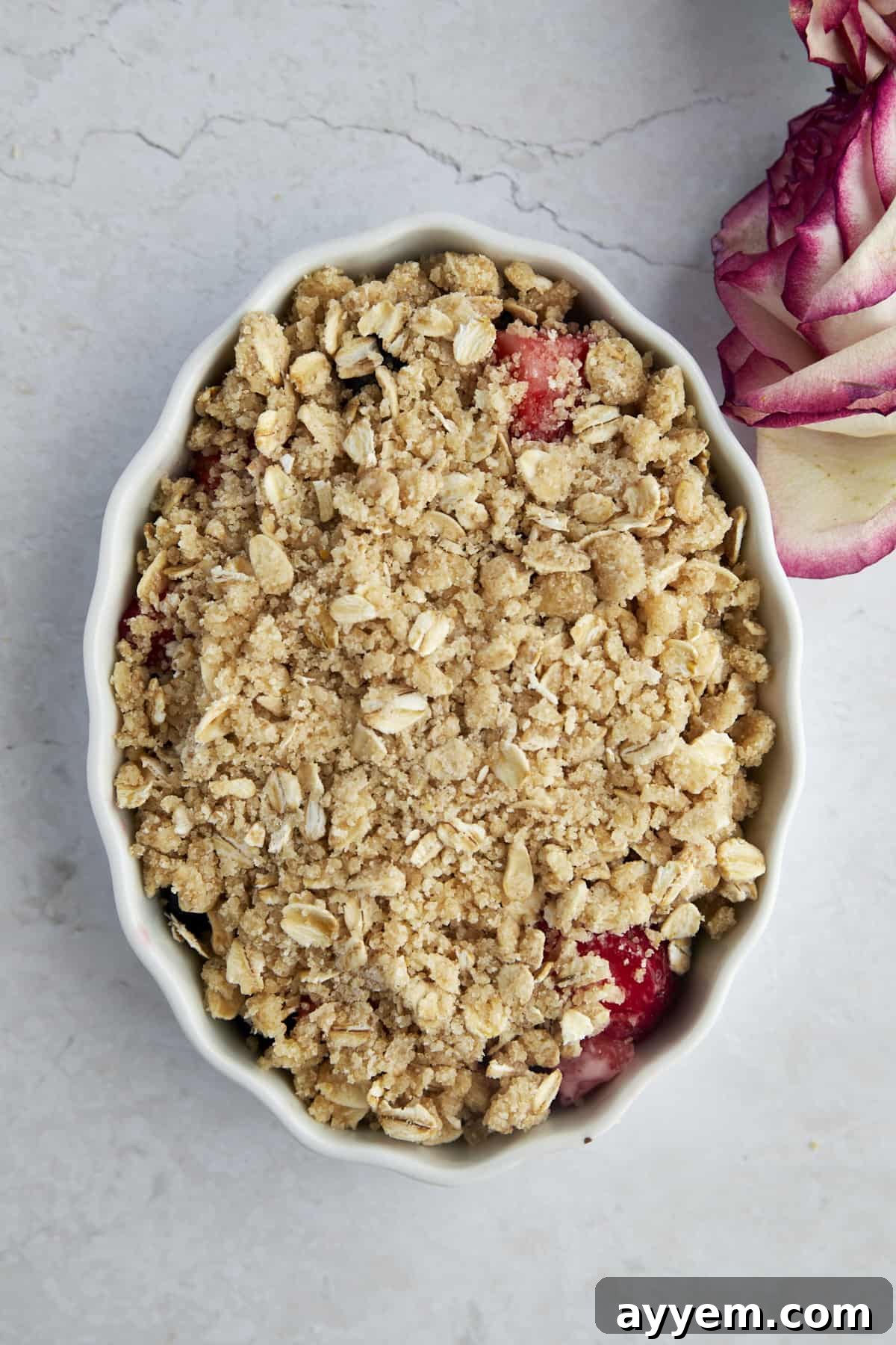 An unbaked mixed berry crisp in a white oval baking dish, with the crumbly topping evenly spread. Ready for the oven.