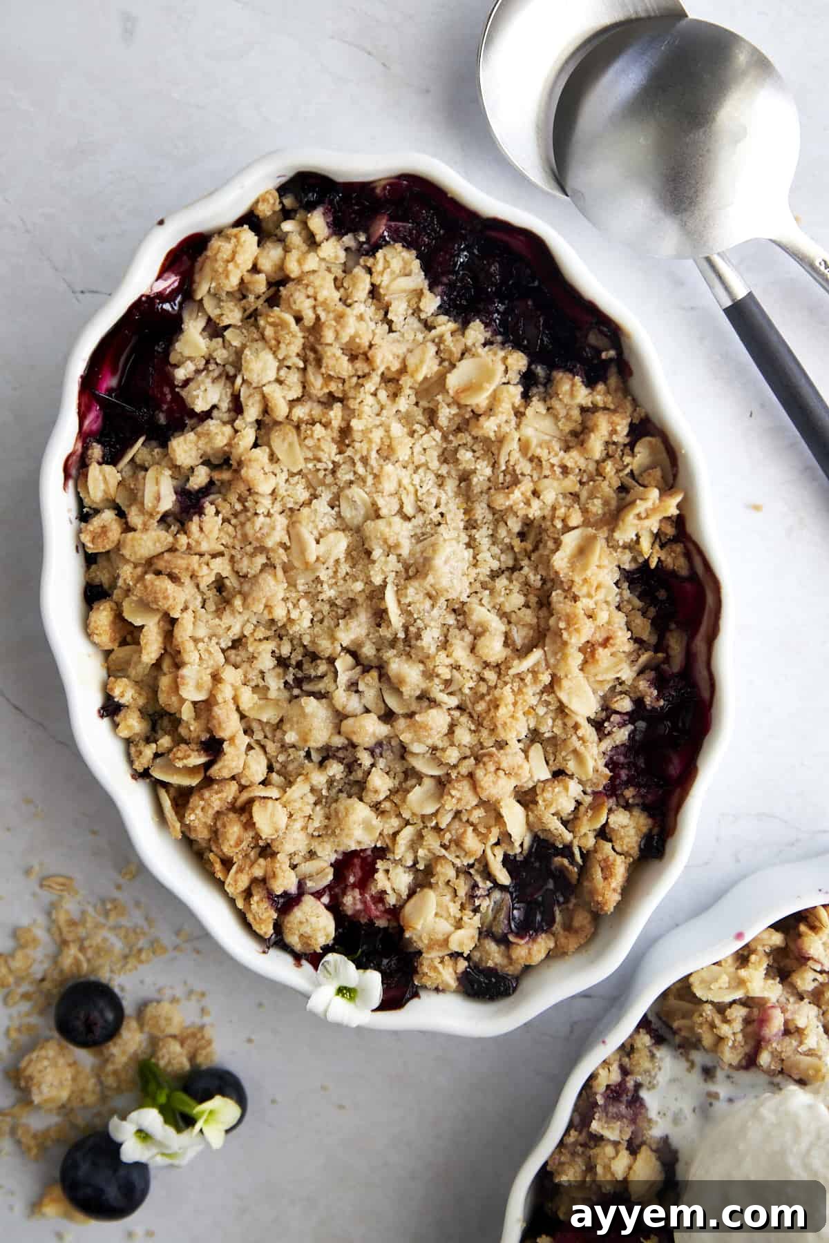 Overhead image of a white oval baking dish full of baked mixed berry crisp. The golden topping and bubbling fruit are visible.