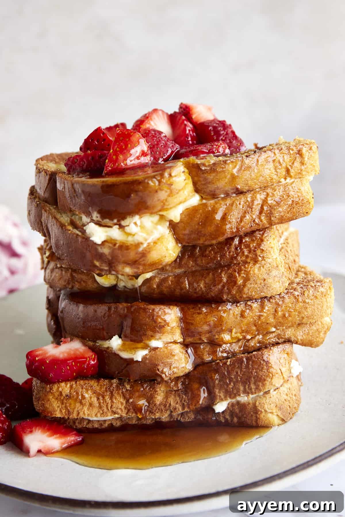 Cream cheese stuffed air fryer french toast sandwiches stacked on top of each other topped with berries and syrup. 