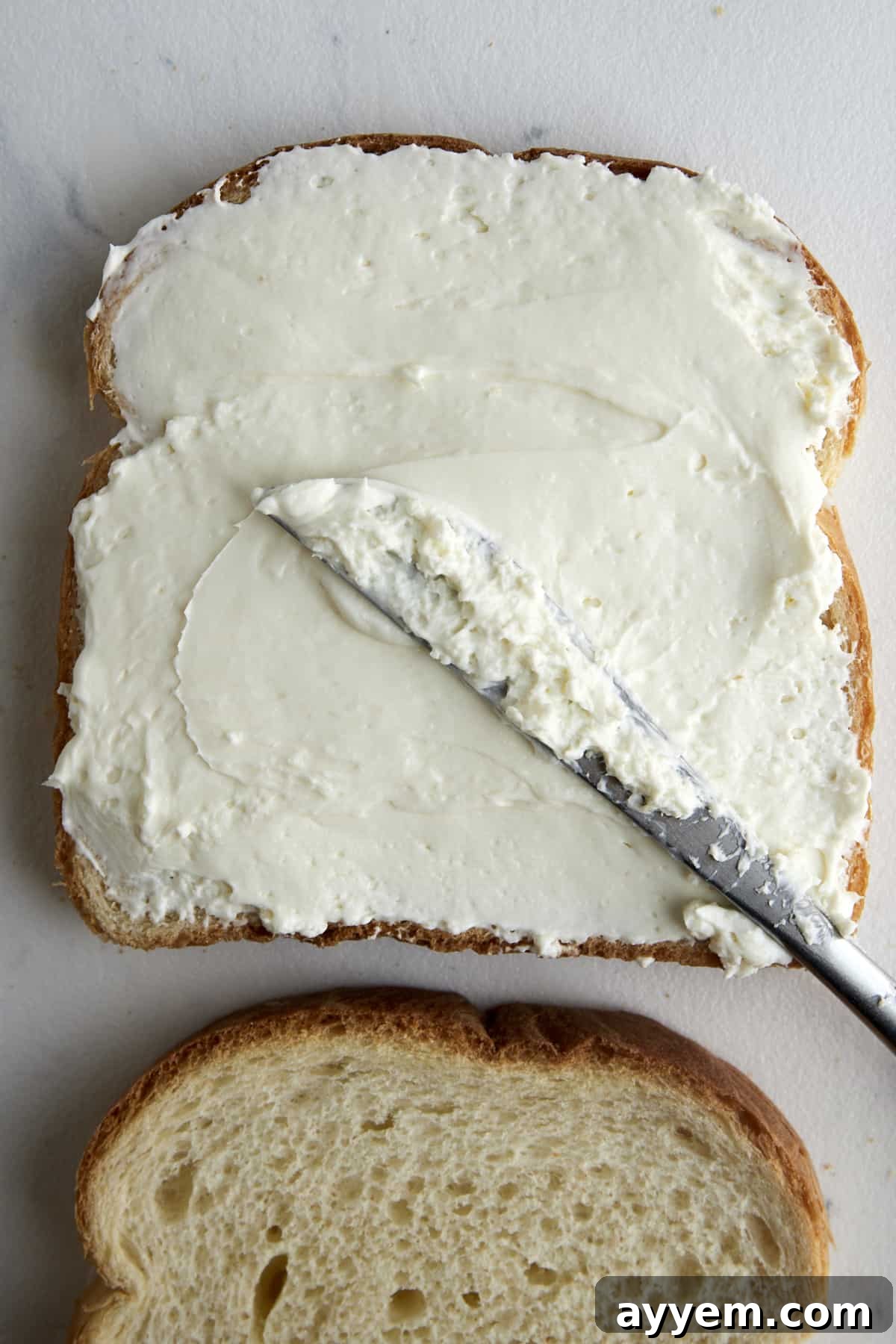 Cream cheese being spread over a piece of bread. 