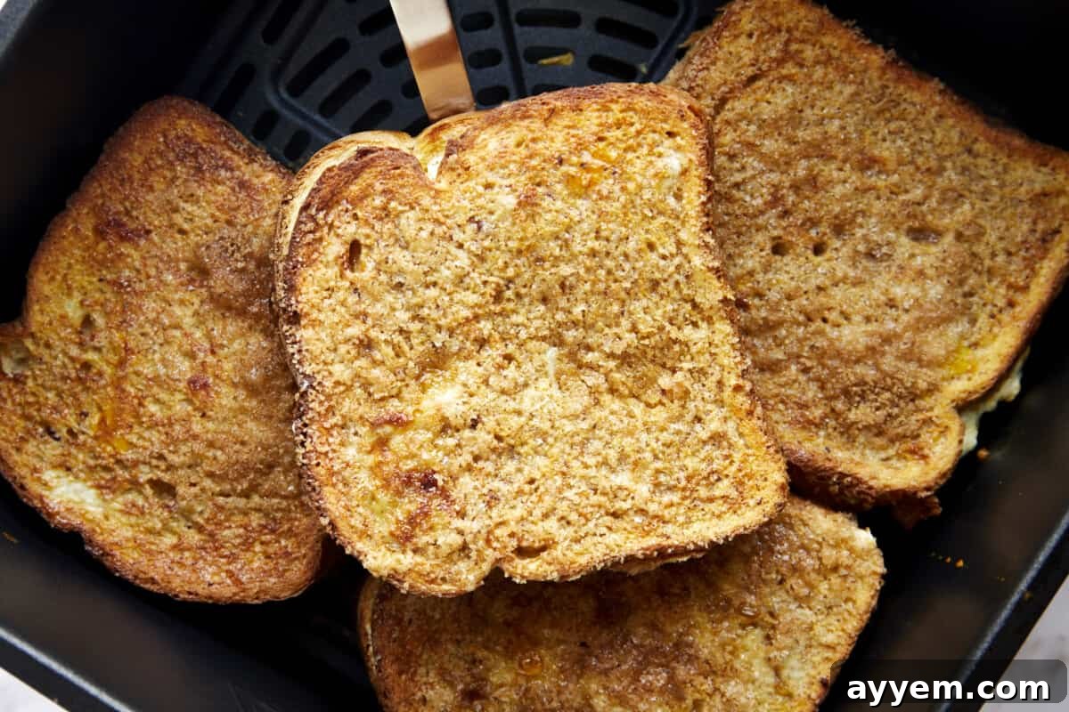 Four cooked cream cheese stuffed air fryer french toast sandwiches in an air fryer basket. 