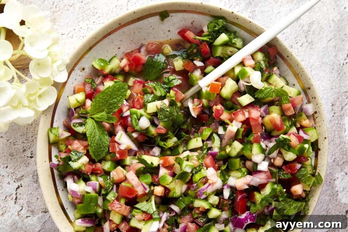 A bowl of Shirazi Salad, freshly dressed and ready to serve, with a spoon for scooping.