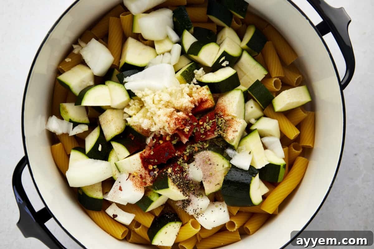 A pot full of rigatoni noodles, zucchini, onion, and spices.