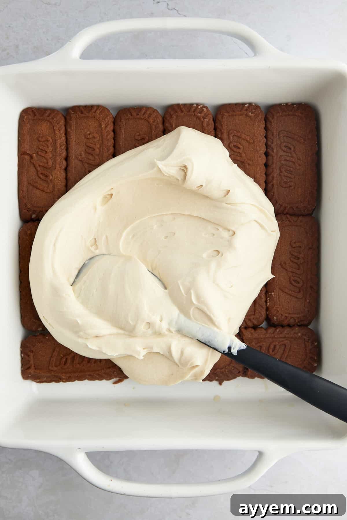 Whipped tiramisu filling being spread over espresso-soaked Biscoff cookies. 