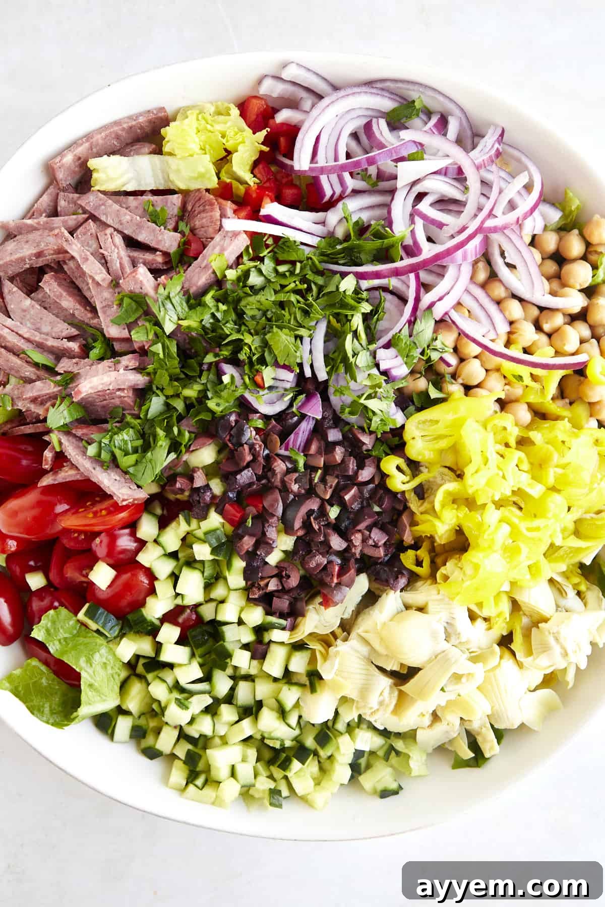 Individual ingredients for an Italian chopped salad recipe arranged in a large bowl, ready for mixing.