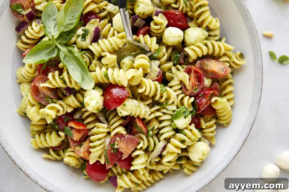 A fork sinking into a bowl of pasta salad with pesto. 