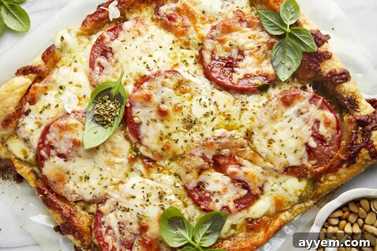 A baked Tomato Pesto Puff Pastry garnished with fresh basil leaves, sliced into servings.