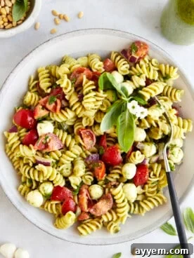 A vibrant bowl of pasta salad with green pesto, cherry tomatoes, and fresh basil, served with a fork.