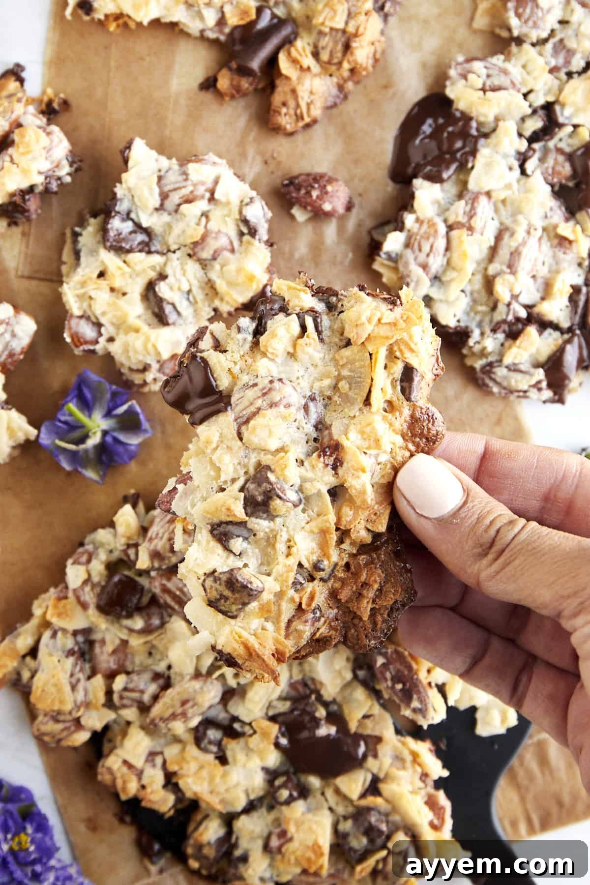 A hand holding a piece of coconut chocolate almond bark, showing the thickness and texture of the chocolate, coconut, and almonds.